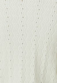 Strikkegenser i off-white med zigzag-mønster, med teksturerte ribber og små åpne masker. Lett materiale, avslappet passform.