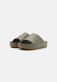 Alyvuogių žalios spalvos slip-on basutės, pagamintos iš minkštos sintetinės medžiagos, su atviru pirštu ir tekstūruotu guminio pado su įpjovomis.