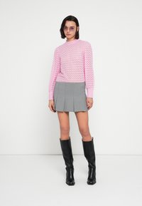 Ροζ πλεκτό πουλόβερ με κυματιστό σχέδιο, συνδυασμένο με γκρι μίνι φούστα με πιέτες. Μαύρες δερμάτινες μπότες μέχρι το γόνατο και μοβ γυαλιά ηλίου ολοκληρώνουν την εμφάνιση.