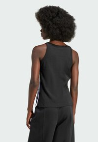 Top senza maniche di colore nero con scollatura rotonda e righe bianche sui lati, realizzato in un morbido tessuto misto cotone.