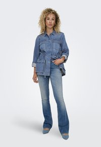 Veste en jean avec deux poches poitrine et taille à cordon de serrage, associée à un jean évasé. Les deux pièces en denim bleu clair avec une texture lisse.