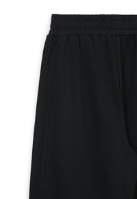 Pantalons de survêtement noirs avec taille élastique, dotés de poches latérales et d'une légère texture. Design simple sans motifs ni embellissements.