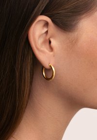 Orecchino a cerchio in oro con finitura liscia e lucida. Il design circolare è di dimensioni medie, con una texture brillante e chiusura senza soluzione di continuità.