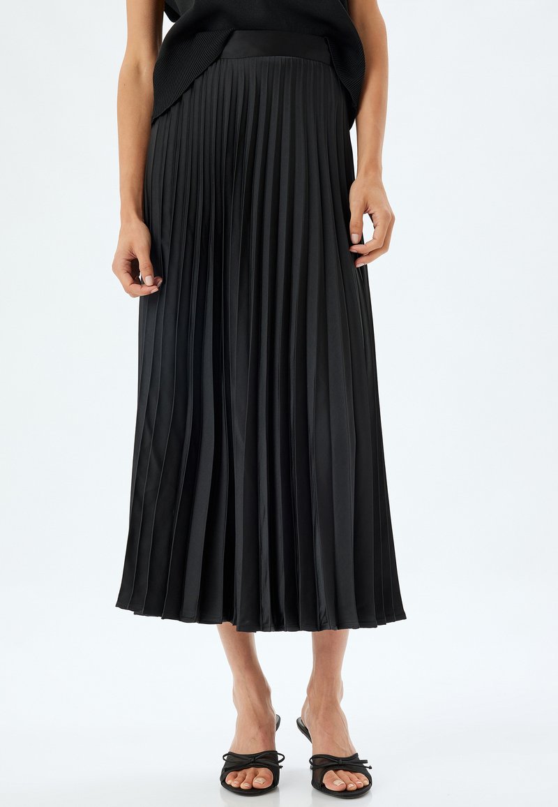 Falda midi plisada negra hecha de material brillante con una cintura ceñida. Presenta pliegues verticales marcados y un diseño fluido.