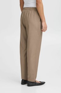 Un pantalon léger, marron, avec coupe décontractée, doté d'une taille élastique et de poches latérales. Des ballerines noires avec une boucle décorative complètent le look.