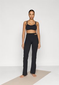 Μαύρο αθλητικό σουτιέν με λεπτές τιράντες και απαλή υφή, συνδυασμένο με μαύρο ψηλόμεσο κολάν που έχει πλαϊνή διακοπή.