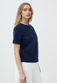 T-shirt a maniche corte di colore blu navy in tessuto morbido con scollatura rotonda, caratterizzato da una vestibilità rilassata e una texture liscia. Abbinato a pantaloni bianchi.