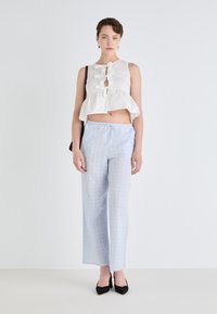 Top bianco a corta lunghezza con fiocchi sul davanti, abbinato a pantaloni larghi blu chiaro con un sottile motivo floreale. Tacchi alti neri.