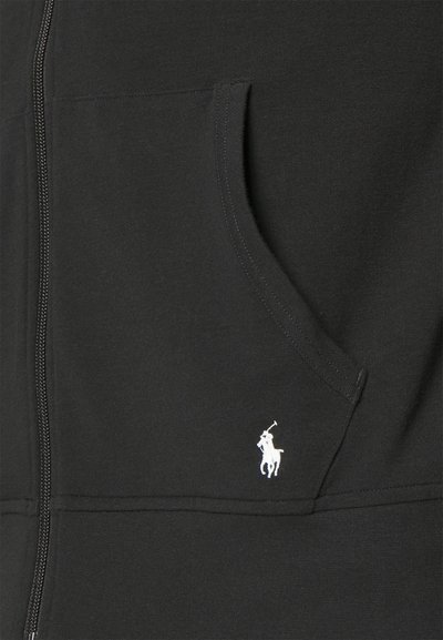 Μαύρο φούτερ με φερμουάρ κατασκευασμένο από μαλακό βαμβάκι. Διαθέτει μπροστινή τσέπη και μικρό λευκό λογότυπο polo στο στήθος. Λείο υφάδι και μινιμαλιστικός σχεδιασμός.