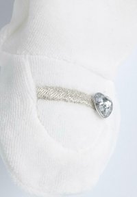 Tessuto di peluche bianco con una texture morbida, caratterizzato da una striscia metallica argento e un accento a forma di cuore in strass vicino al bordo.