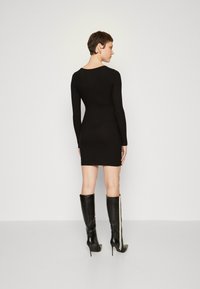 Crna dugosleeve bodycon haljina s okruglim izrezom, glatke teksture i prilagođenog dizajna, uparena s crnim čizmicama do koljena s bijelim prugama.