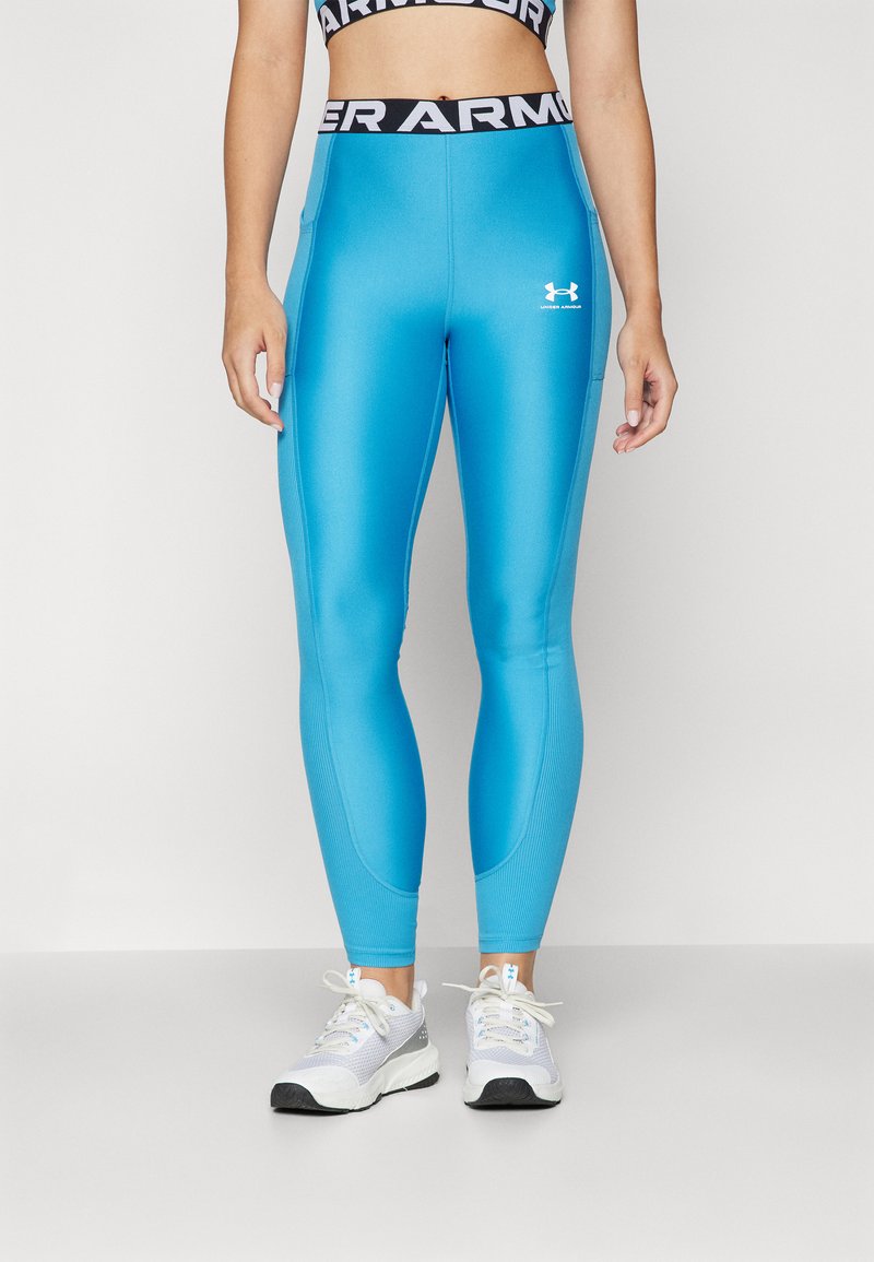 Modre atletske leggins hlače, narejene iz gladkega, raztegljivega materiala. Imajo črn pas z logotipom "UNDER ARMOUR" na pasu. Prilagojena zasnova, dolžina do gležnjev.