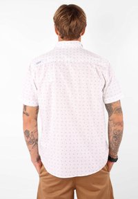 Chemise blanche à manches courtes avec un petit imprimé bleu, col boutonné et empiècement au dos. Présente une étiquette en haut du dos. Texture lisse.