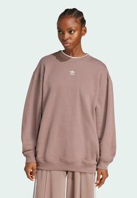 Felpa oversize color malva realizzata in morbido tessuto. Presenta un colletto e polsini a coste, con un piccolo logo bianco adidas sul petto.