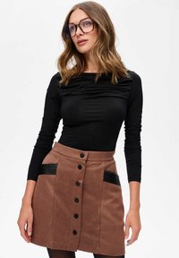 Zwarte longsleeve top met rimpeling, gecombineerd met een bruine rok met zwarte neplederen accenten en zwarte knoopsluitingen.