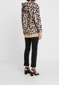 Felpa con stampa leopardata in beige con macchie nere, abbinata a jeans neri a gamba slim e sandali neri con tacco, dotati di cinturini alla caviglia e tacchi robusti.
