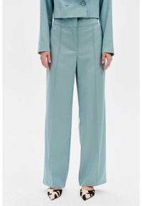Pantalons ajustés bleu clair avec une coupe à jambes larges, présentant des lignes épurées et une texture lisse, accompagnés de chaussures à bout pointu dans un motif animal contrasté.