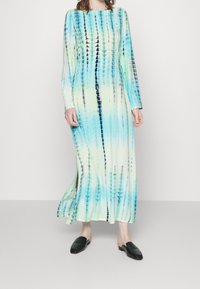 Dlouhé rukávy, šaty s technikou batikování v odstínech modré a zelené. Hladká látka, s návrhem do kotníků a bočními rozparky. Nosit s černými mulemi.