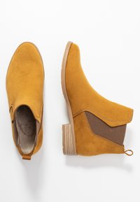 Stivaletti alla caviglia in suede giallo con pannello laterale testurizzato, punta rotonda e tacco basso a blocco; linguetta ad anello sul retro per indossarli facilmente.