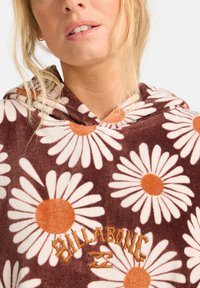 Sudadera con capucha de tejido de terciopelo marrón que presenta grandes margaritas blancas con centros naranjas; "BILLABONG" bordado en naranja en la parte delantera.