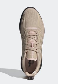 Beige athletic shoe with mesh upper, tonal three stripes, pink accents on laces and heel, black outsole, and textured detailing.