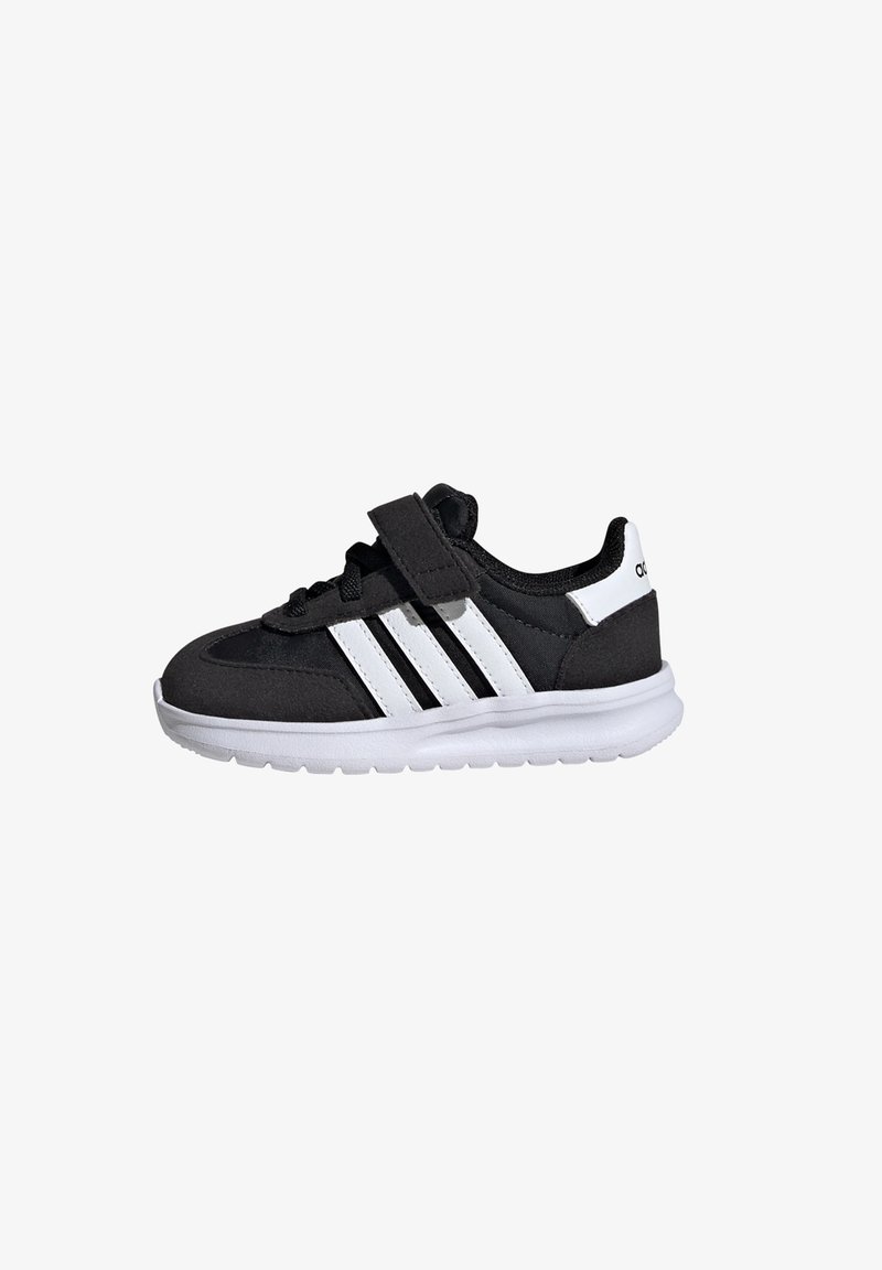 Zapatilla deportiva negra con acentos blancos, que cuenta con una correa de Velcro, diseño de tres rayas, suela acolchada y parte superior de tela texturizada.