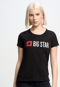 Juodas medvilnės marškinėliai trumpomis rankovėmis, su raudonu kvadratu ir balta užrašu "BIG STAR" ant priekinės pusės. Lygus paviršius.