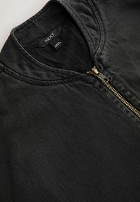 Schwarze Jeansjacke mit einem geschlossenen goldenen Reißverschluss und rundem Kragen, innen am Halsausschnitt ist ein "NEXT" Markenlabel zu sehen.