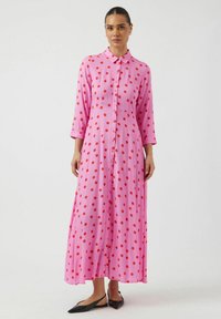 Rosa maxikjole med røde prikker, knappelukking foran og krage. Har trekvartlange ermer og en flytende passform. Teksturert stoff.