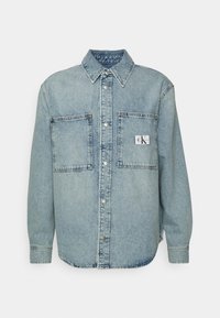 Světle modrá džínová košile s dlouhými rukávy, patentní knoflíky, dvěma náprsními kapsami a štítkem CK na levé kapse. Klasický design límce.