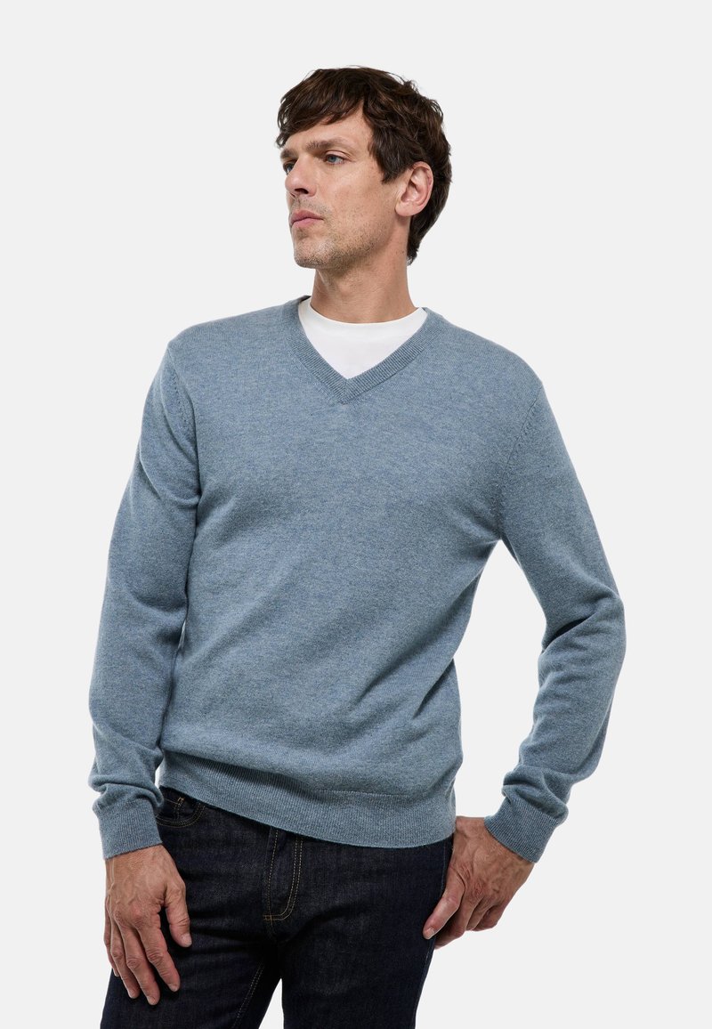 Pull bleu clair en V en tissu doux, avec des poignets et un ourlet côtelés, superposé sur un t-shirt blanc, associé à un jean foncé.