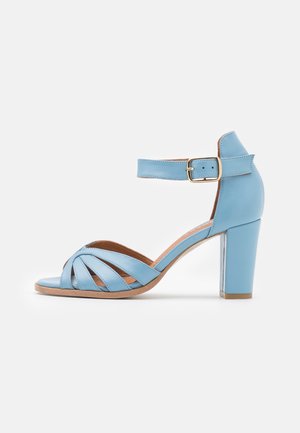 Light blue leather high-heeled sandal with an open toe, ankle strap, and multiple crisscross bands on the front. Square, chunky heel.