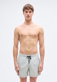 Ανοιχτό γκρι μαγιό βερμούδα με ελαστική μέση και μαύρο κορδόνι, κοντό μήκος, με λεία υφή και χωρίς ορατά σχέδια.