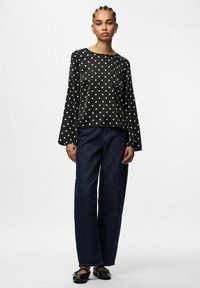 Top negro con lunares, de manga larga y corte holgado, combinado con jeans de mezclilla oscuros de pierna ancha y zapatos planos negros.