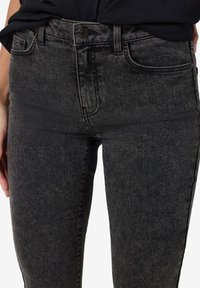 Tamsiai pilki slim-fit džinsai pagaminti iš džinsinio audinio, turintys šiek tiek nudilusią tekstūrą. Pasižymi klasikinio penkių kišenių dizainu ir mygtukų užsegimu.