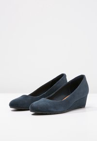Décolleté in suede blu scuro con zeppa, punta arrotondata e texture liscia, caratterizzati da un tacco leggermente elevato e un design minimalista.