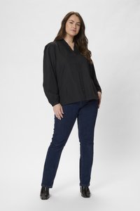 Blusa negra de botones con un escote con volantes, combinada con jeans azul oscuro y botas negras hasta el tobillo. Tejido suave, corte relajado, mangas largas.