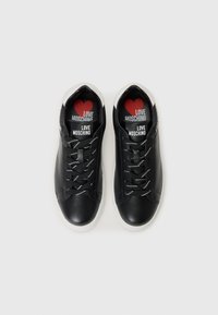 Black low-top sneakers with white soles and black laces, logos on tongue and insoles reading "Love Moschino" with a red heart.