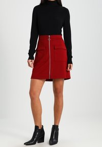 Rød nederdel med en lynlås foran, to store lommer og en udvidet form, parret med en sort turtleneck og sorte ankelstøvler.