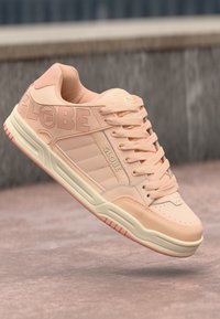 Light pink sneaker with a textured leather upper, embossed "GLOBE" branding, woven laces, and a cream rubber sole with ribbed accents.