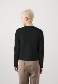 Μαύρο πλεκτό πουλόβερ με στρογγυλή λαιμόκοψη, μακριά μανίκια, υφασμένο ύφασμα και εφαρμοστή σχεδίαση, συνδυασμένο με μπεζ παντελόνι ψηλής μέσης.