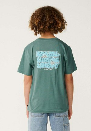 Persona con cabello rizado que lleva una camiseta verde de Rip Curl Surfing Company y vaqueros azul claro, vista desde atrás.