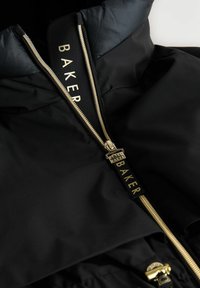 Sort jakke med høj krave, guld lynlås og mærkeetiket. Materialet ser glat og vandafvisende ud med en subtil tekstur.