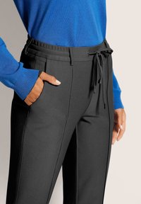 Zwarte broek van gestructureerde stof met een trekkoord in de taille, zijzakken en strakke lijnen, gecombineerd met een blauwe trui.