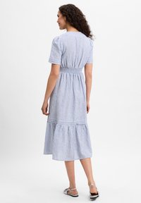 Gestreiftes Baumwoll-Midikleid mit kurzen Ärmeln, gerafftem Taillenteil und gestuftem Saum. Hellblau und weißes Farbschema. Flache Sandalen sichtbar.