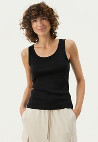 Sort ærmeløs tanktop lavet af tekstureret bomuld, med en rund halsudskæring og bølget kant. Sammen med lysebeige bukser.