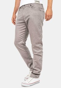 Lichtgrijze geweven broek met een slim fit, voorzien van een knoopsluiting, steekzakken en een subtiele textuur. Gecombineerd met witte sneakers.