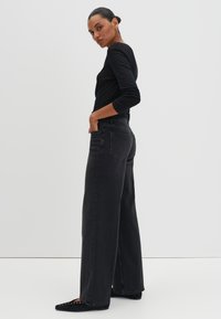 Jean en denim noir taille haute avec une coupe large, dotés de poches arrière et d'une texture mate lisse. Associé à un haut noir ajusté à manches longues.