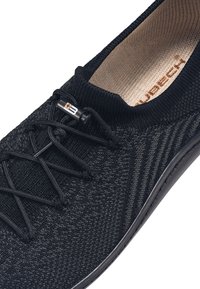 Czarne dzianinowe buty sportowe z teksturowaną cholewką, elastycznymi sznurowadłami i okrągłą pętelką do zakupu. Wnętrze ma beżową wkładkę z logo marki.