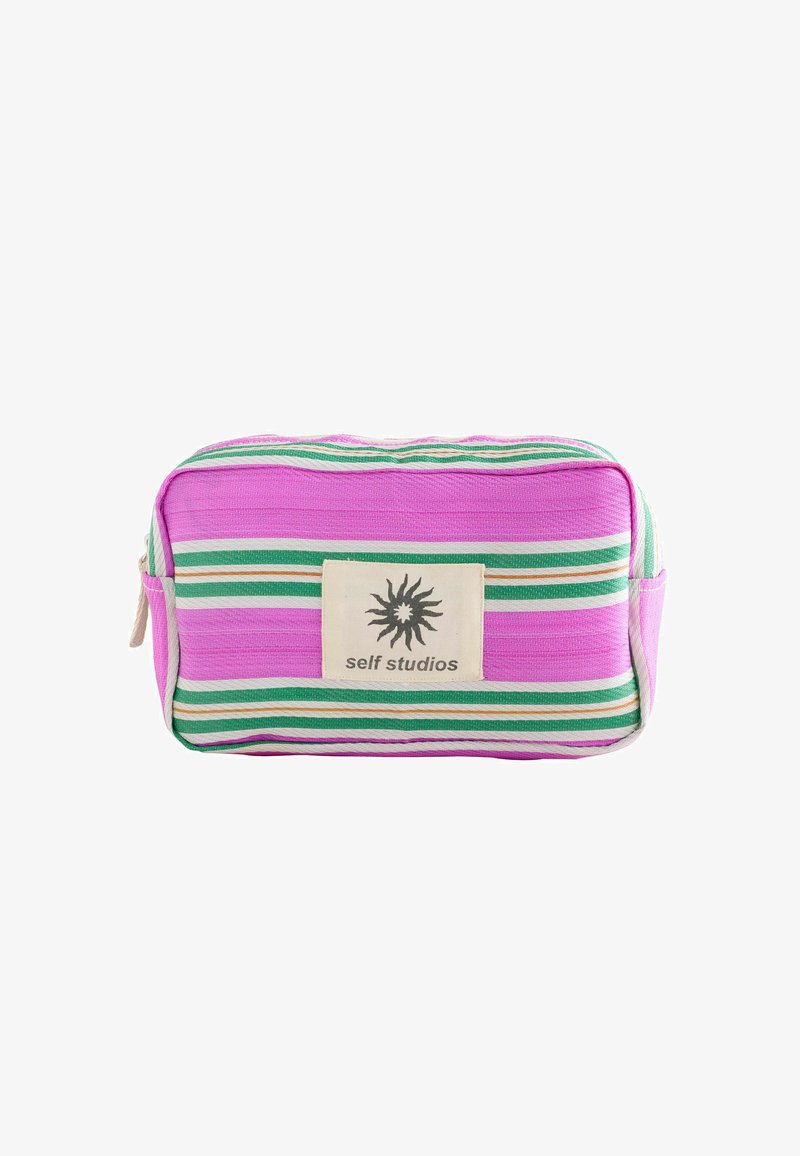 Pochette rectangulaire en tissu rose avec des rayures vertes, blanches et orange, fermeture éclair, et un patch logo "self studios" à l'avant.